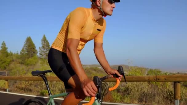 Tracking shot van de video van een mannelijke wielrenner klimmen op een bergweg. Man doet fietsen training op een heuvelachtig snelweg weg op een zonnige dag. — Stockvideo
