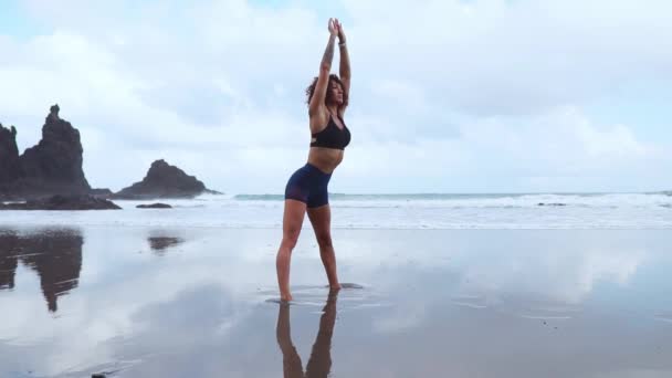 La muchacha hace el calentamiento antes de hacer los deportes temprano en la mañana en la orilla del mar. Una chica de constitución atlética con una masa muscular seca . — Vídeos de Stock