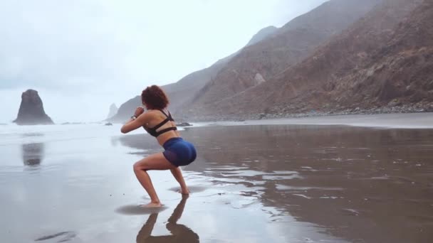 Hermosa chica atlética en ropa deportiva en el océano después de la marea baja haciendo ejercicios para calentar y tonificar los músculos. El concepto de un estilo de vida saludable. Yoga — Vídeos de Stock