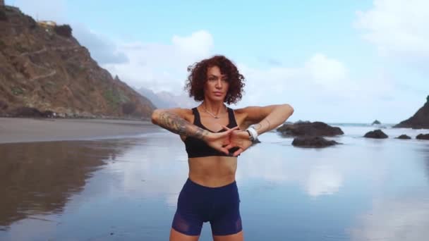 Aptitud y motivación. Chica atleta saludable estirándose en la playa en un día soleado. Mujer deportiva con trenza calentando sus piernas antes de hacer ejercicio al aire libre. Fit mujer haciendo yoga en la playa — Vídeo de stock