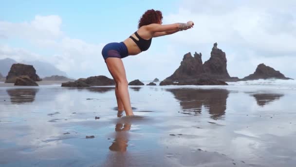 Aptitud y motivación. Chica atleta saludable estirándose en la playa en un día soleado. Mujer deportiva con trenza calentando sus piernas antes de hacer ejercicio al aire libre. Fit mujer haciendo yoga en la playa — Vídeos de Stock