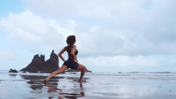 Hermosa chica atlética en ropa deportiva en el océano después de la marea baja haciendo ejercicios para calentar y tonificar los músculos. El concepto de un estilo de vida saludable. Yoga. Meditación y relajación — Vídeos de Stock