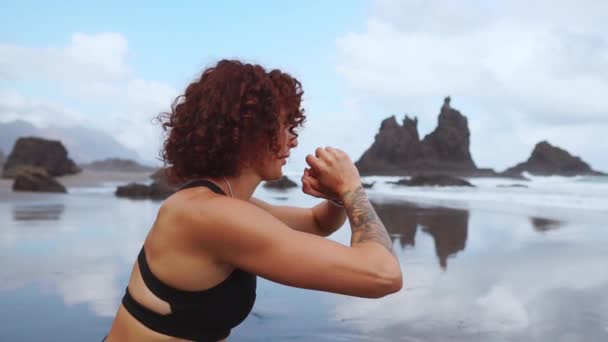 바다의 해변에 스포티 한 옷에 아름 다운 운동 소녀가 라오를 수행합니다. 건강 한 생활양식입니다. 피트 니스 — 비디오