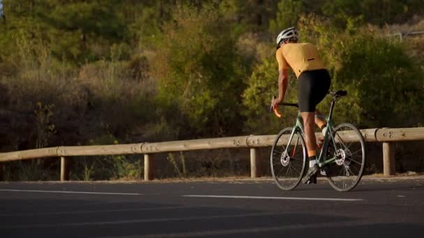 Ciclista profesional en un casco y equipo deportivo paseos en una carretera de montaña — Vídeos de Stock