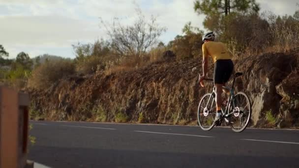Un cycliste professionnel dans un casque et des promenades d'équipement sportif sur une serpentine de montagne au coucher du soleil en direction du volcan. Steadicam — Video