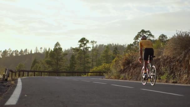 Un ciclista profesional en casco y equipo deportivo monta en una serpentina de montaña al atardecer en dirección al volcán. Steadicam — Vídeo de stock