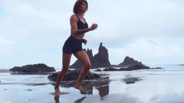 Девушка бежит по черному вулканическому песку в океане в замедленной съемке — стоковое видео