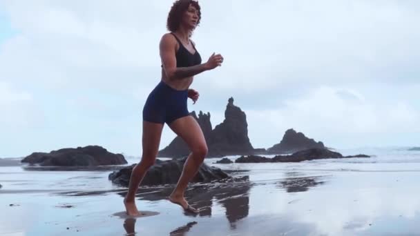 Fille courir sur le sable volcanique noir sur l'océan au ralenti — Video