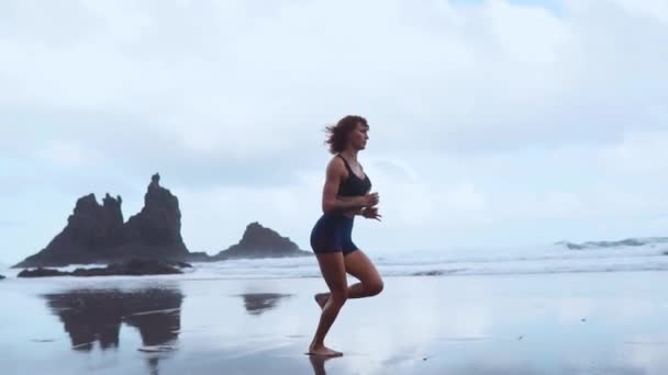 Sportowe kobieta działa na plaży z czarnym piaskiem, na tle góry i ocean w zwolnionym tempie. Wyspy Kanaryjskie. Ocean Atlantycki — Wideo stockowe