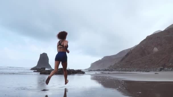 Sportowe kobieta działa na plaży z czarnym piaskiem, na tle góry i ocean w zwolnionym tempie. Wyspy Kanaryjskie. Ocean Atlantycki — Wideo stockowe
