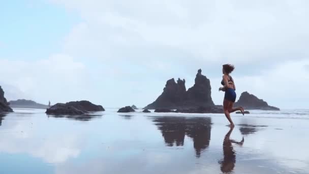 Kobieta działa na czarnym wulkanicznym piaskiem na Wyspach Kanaryjskich, na tle zamrożone magmy. Pojęcie zdrowego stylu życia. Zwolnionym tempie. — Wideo stockowe