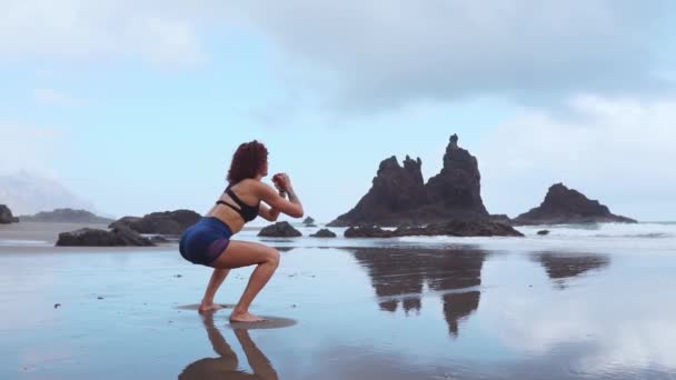 Una mujer hace sentadillas en las orillas del océano Atlántico. El concepto de un estilo de vida saludable. Practicar deportes en Canarias — Vídeos de Stock