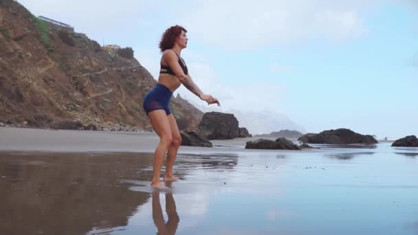 Una mujer hace sentadillas en las orillas del océano Atlántico. El concepto de un estilo de vida saludable. Practicar deportes en Canarias — Vídeos de Stock