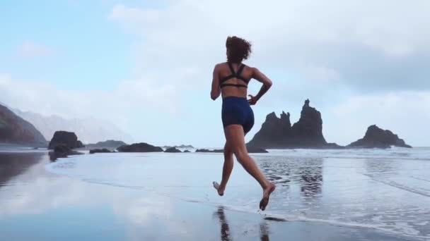 Chica deportiva descalza con cuerpo delgado corriendo a lo largo del mar surf junto a la piscina de agua para mantenerse en forma y la salud. Fondo de playa con cielo azul. Mujer fitness, actividad deportiva de jogging en vacaciones familiares de verano . — Vídeo de stock