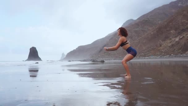 Saltar sentadillas - Ajuste piernas de entrenamiento de mujer con ejercicios de sentadillas de salto de entrenamiento de hiit. Entrenamiento de fitness haciendo ejercicio cardiovascular en verano playa de arena blanca haciendo saltos explosivos para activar los glúteos . — Vídeos de Stock