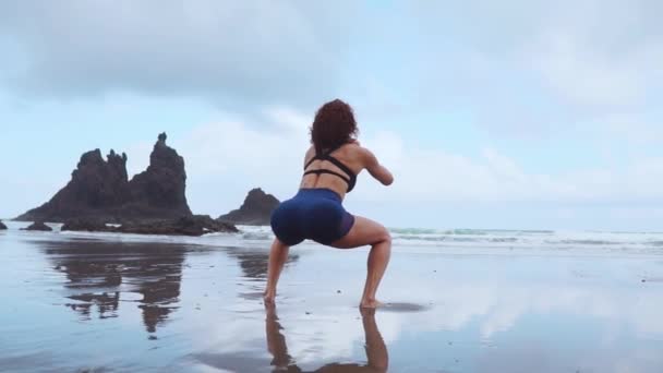 Una mujer hace sentadillas en las orillas del océano Atlántico. El concepto de un estilo de vida saludable. Practicar deportes en Canarias — Vídeos de Stock