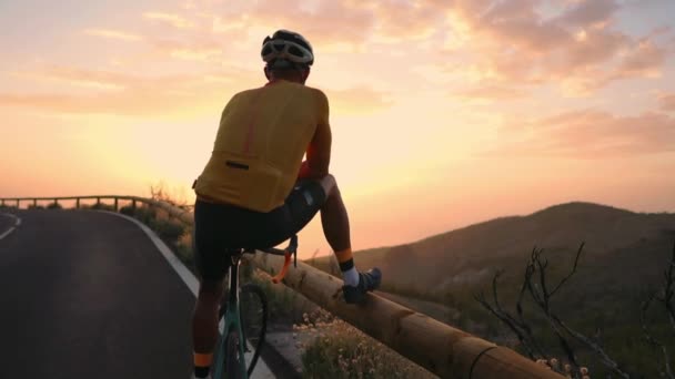 Homem ciclista em uma camiseta amarela nas montanhas assistindo o pôr do sol. Descansando depois de um treino, homem de ferro — Vídeo de Stock