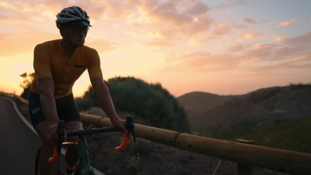 Hombre ciclista en camiseta amarilla monta una bicicleta de montaña al atardecer en la carretera — Vídeo de stock