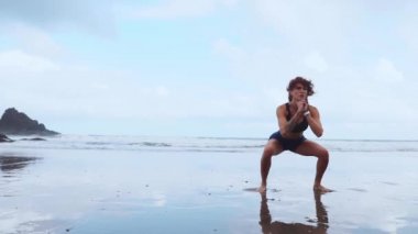 Zıplama egzersizleri yaparak bacak çalıştıran sağlıklı bir kadın. Spor salonu yaz aylarında kardiyo egzersizi yapıyor. Beyaz kumlu plajda. Kalça kaslarını çalıştırmak için sıçrama ve geğirme hareketleri yapıyor..