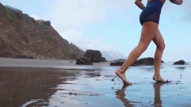Etkin sportif kadın okyanus sörf zinde ve Sağlık tutmak için su havuzu tarafından çalıştırın. Günbatımı siyah kum plaj güneş ile arka plan. Kadın fitness, egzersiz ve spor etkinliği yaz aile tatil koşu.