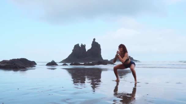 Hoppa knäböj - Fit kvinna utbildning ben med hiit träning hoppande knäböj övningar. Konditionsträning gör konditionsträning på sommaren ocean vit sandstrand gör explosiva hopp för att aktivera glutes. — Stockvideo