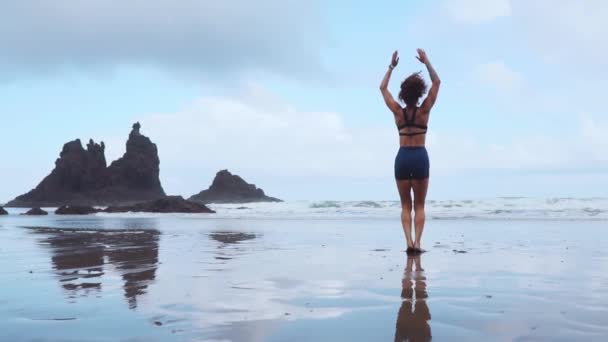 Dziewczynie skaczącej burpee treningu czarnej, piaszczystej plaży w pobliżu ocean Atlantycki z górami w tle — Wideo stockowe