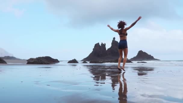 Lány jumping burpee edzés a fekete homokos strand közelében az Atlanti-óceánra, a hegyek a háttérben — Stock videók