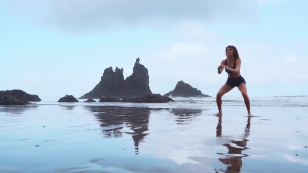跳蹲适合妇女训练腿与 hiit 锻炼跳蹲练习。健身训练做有氧运动在夏季海洋白色沙滩做爆炸性跳跃激活臀部. — 图库视频影像