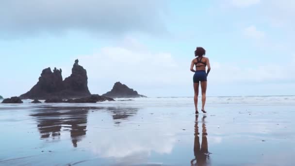 Mujer deportiva activa correr a lo largo del océano surf junto a la piscina de agua para mantenerse en forma y la salud. Atardecer arena negra playa de fondo con sol. Mujer fitness, ejercicio de jogging y actividad deportiva en vacaciones familiares de verano . — Vídeo de stock