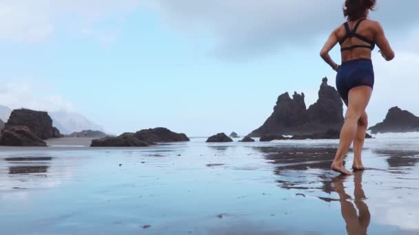 Donna sportiva attiva correre lungo l'oceano surf da piscina d'acqua per mantenersi in forma e la salute. Tramonto sabbia nera sfondo spiaggia con sole. Fitness femminile, allenamento di jogging e attività sportive durante le vacanze estive in famiglia . — Video Stock