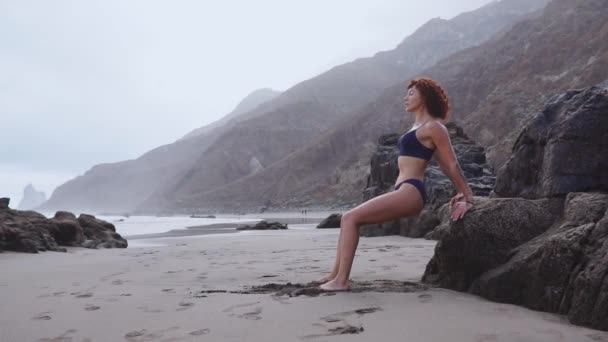 Mujer haciendo flexiones en una roca en la playa cerca del océano. Fitness mujer joven haciendo flexiones en la playa — Vídeo de stock