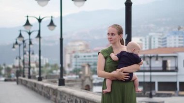 Genç Anne oğlu bebeği ile okyanusu Europe bakar, gülümser ve dalgalar antik meydanında yakın sahildeki yürür