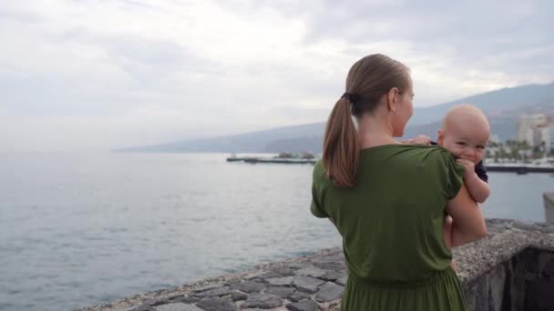 Una giovane mamma con un bambino spara sulle mani guardando l'oceano e la vista mozzafiato delle onde. Mostra le navi bambino in lontananza . — Video Stock