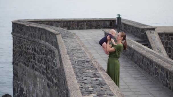 Jeune mère joue avec son fils bébé sur le front de mer près de l'océan sur l'ancienne place de l'Europe . — Video