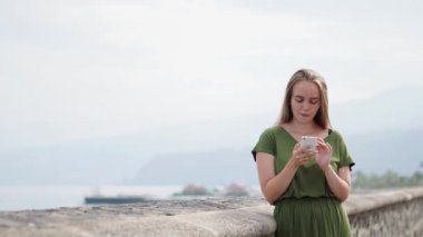 Hippi kız sırt çantası ile akıllı telefon gadget kum kıyı şeridi'dur. Gezgin el arka plan plaj deniz manzarası ufukta telefon kullanarak. Mavi güneş okyanus, yaz yaşam tarzı turist bak