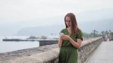 Hippi kız sırt çantası ile akıllı telefon gadget kum kıyı şeridi'dur. Gezgin el arka plan plaj deniz manzarası ufukta telefon kullanarak. Mavi güneş okyanus, yaz yaşam tarzı turist bak