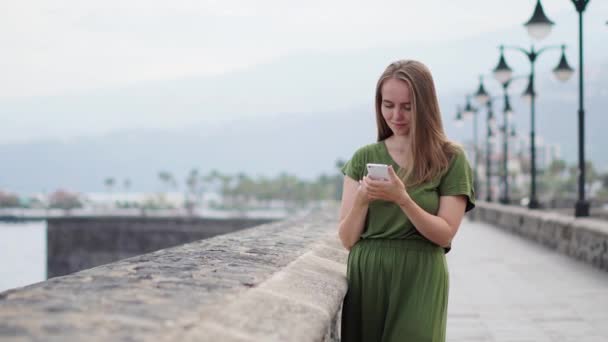 Hipster girl with backpack hold on smart phone gadget in sand coastline. Traveler using in female hand mobile on background beach seascape horizon. Tourist look on blue sun ocean, summer lifestyle — Stock Video