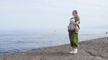 Bebek ve anne yaz gün denizde üzerinde. Mutlu bir aile doğa açık havada yürüyüş. Çocuk bir taşıyıcı sırt çantası içinde. Kadın ve bebeğinin adanın Tenerife, İspanya'nın kıyı şeridi okyanus üzerinde. Avrupa'yı gezersin