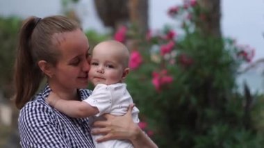 Çocuk annesine bir hugs çalış ve palmiye ağaçları çiçek Resort ile bebeği öper. Mutlu bir aile