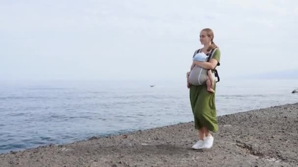 Baby en moeder op zee bij zomerdag. Wandelen op de natuur buiten en gelukkige familie. Kind in de rugzak van een vervoerder. Vrouw en haar baby op oceaan van de kust op het eiland Tenerife, Spanje. Reizen Europa — Stockvideo