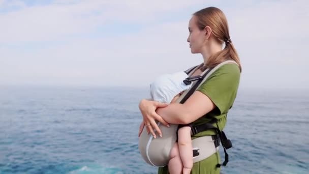 Baby en moeder op zee bij zomerdag. Wandelen op de natuur buiten en gelukkige familie. Kind in de rugzak van een vervoerder. Vrouw en haar baby op oceaan van de kust op het eiland Tenerife, Spanje. Reizen Europa — Stockvideo