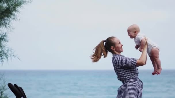 Счастливая семья. Молодая мать бросает ребенка в небо, в солнечный день. Портрет мамы и маленького сына на пляже. Положительные человеческие эмоции, чувства, радость . — стоковое видео
