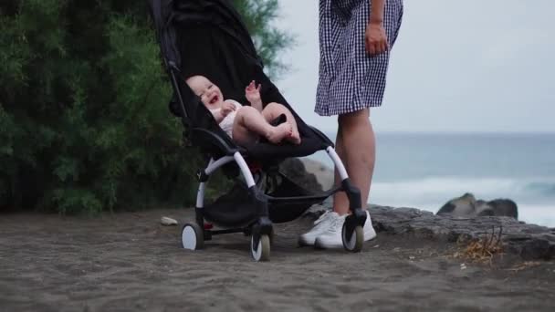 Side view of young mother pushing baby stroller over summer beach background — Stock Video