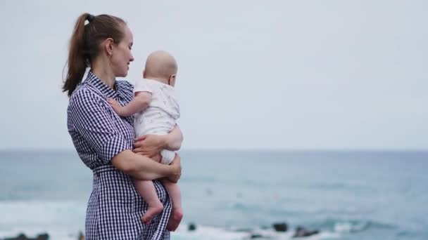 Anne öpücük kız deniz ve plaj arka plan üzerinde güzel portresi. Mutlu aile tatil. Seyahat. Annem günbatımı üzerinde yürümeye başlayan çocuk sarılmak. Okyanus dışında bebeğe beyaz kadın var. Annelik Bakımı. — Stok video