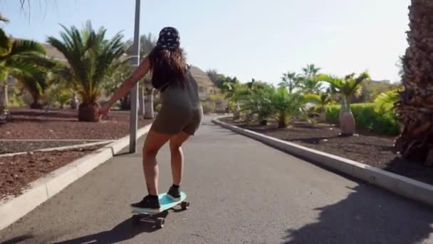 Красивая молодая девушка едет по дороге рядом с пляжем и пальмы на длинной доске в замедленной съемке — стоковое видео