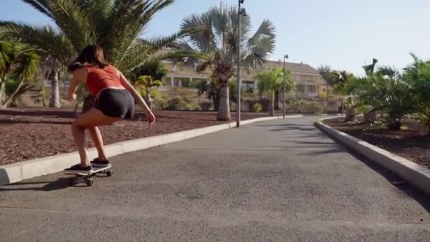 Mladá dívka jezdí na silnici poblíž palmy na longboard v pomalém pohybu — Stock video