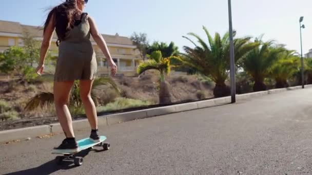 Dziewczyna na deskorolce w krótkie spodenki jeździ na drodze wzdłuż plaży i palm drzew — Wideo stockowe