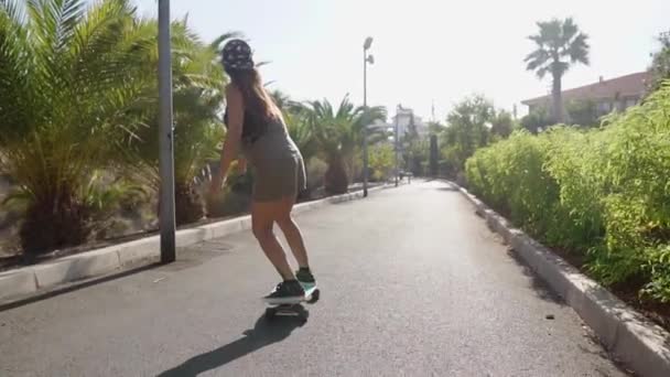 Piękna młoda dziewczyna jeździ na drodze w pobliżu plaży i palm drzew na longboard w zwolnionym tempie — Wideo stockowe