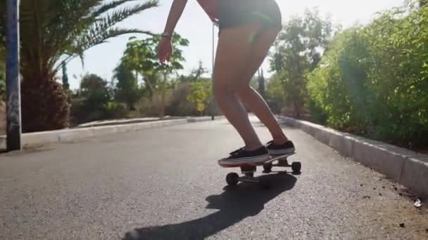 Summer on the island girl on longboard rides in short shorts on the road near the beach and palm trees — Stock Video