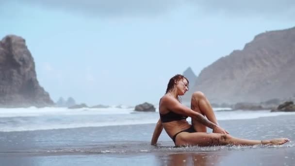 바다에 체조에 종사 하는 여자는 삼 실에 앉아서 파도 대 한 물 근처 다리를 수행 하 고. 요가 연습. 건강 한 생활양식입니다. 스트레칭 — 비디오